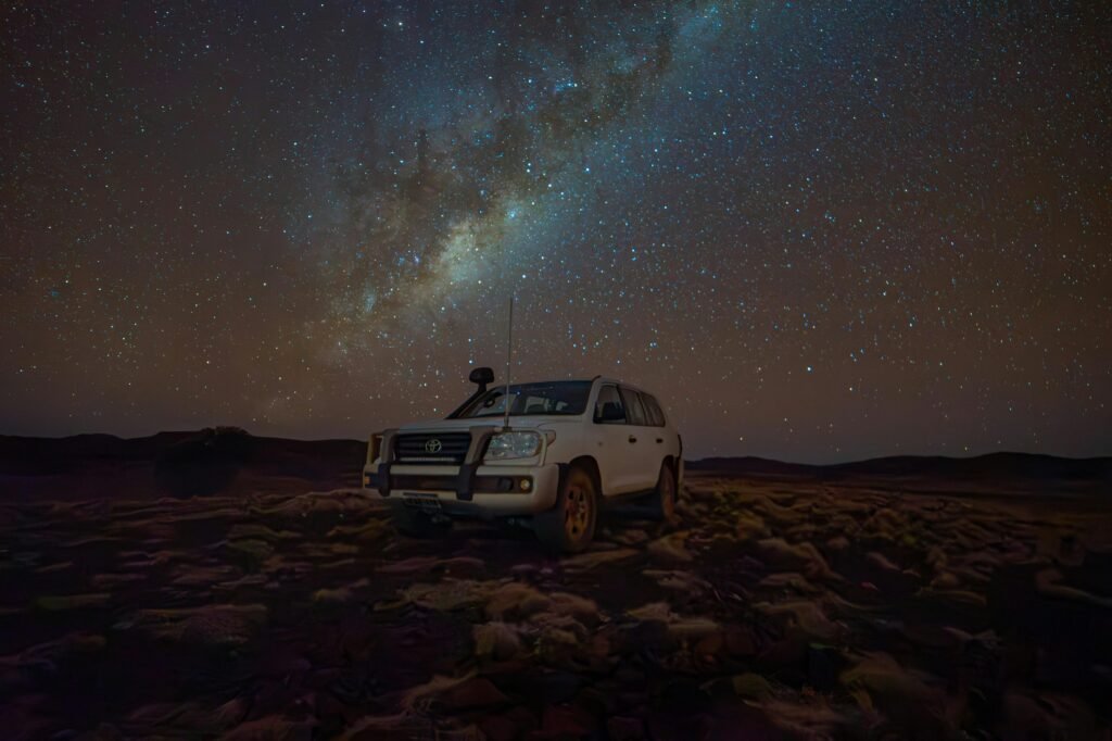 A Toyota Land Cruiser parked under a star-filled night sky in a rural setting.