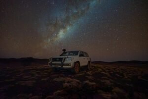 A Toyota Land Cruiser parked under a star-filled night sky in a rural setting.